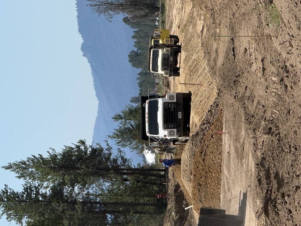 Dump trucks placing road material on a jobsite with mountains behind