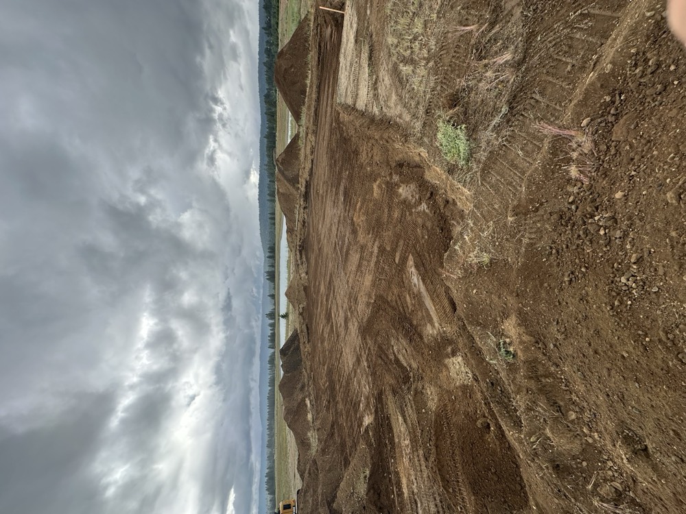 Graded building pad with stockpiles under storm clouds