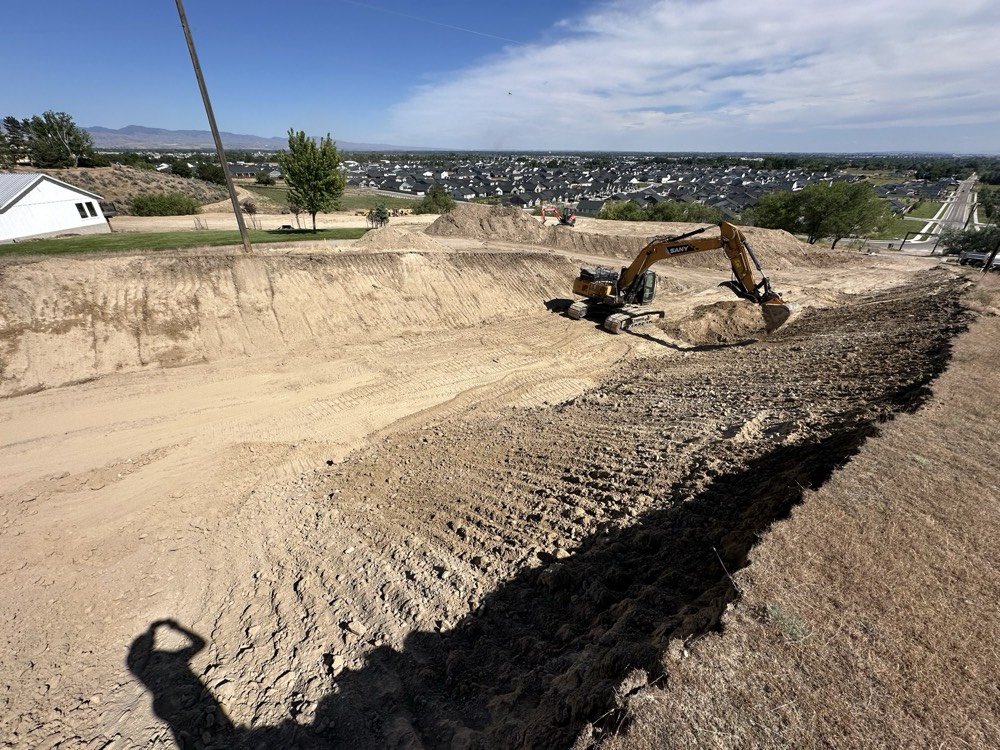 Excavator cutting a road through a foothill above a valley town