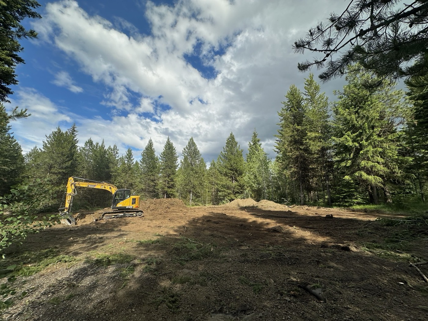 Cleared building lot with an excavator among pines under a blue sky in McCall, Idaho
